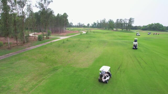 Drone view of group of golfers riding together in golf cart on course.
