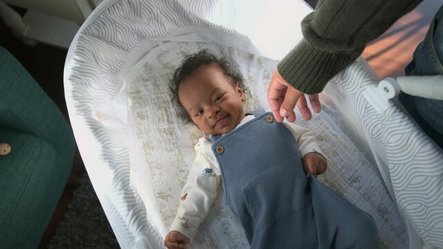 Happy adorable newborn baby lies in a cozy bassinet reaching toward an adult hand while smiling warmly creating a tender home moment with soft natural light and a calm relaxed atmosphere