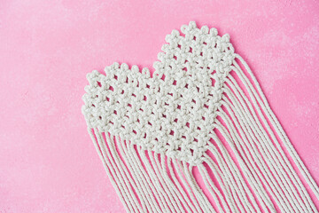 Heart shaped macrame piece with long fringe on pink background