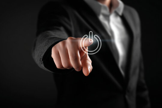 Businessman hand pointing to activate a glowing power on/off symbol. Concept of start, new beginnings, technology, and digital energy on a virtual interface