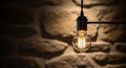 Illuminated vintage light bulb hanging against a rustic stone textured wall background creating