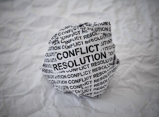 Crumpled paper ball with words Conflict Resolution on crumpled white paper background.