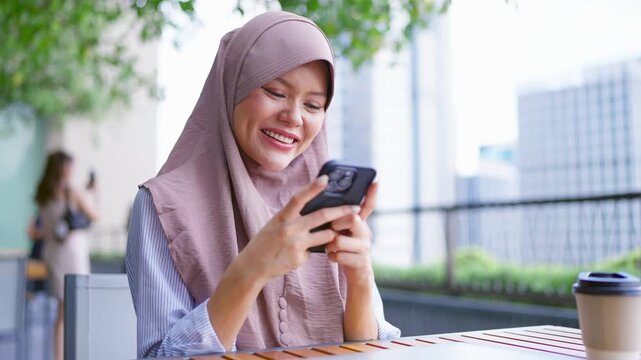 Asian Muslim businesswoman using mobile phone outdoors in the city. 