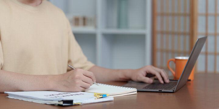 Work from Home: Close-up of young man writing notes while using laptop