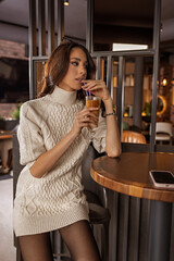 Beautiful young woman in a short wool dress standing alone and drinking coffee