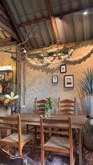 A cozy, retro-inspired lounge area in a coffee shop features a set of four wooden tables and chairs, earth-colored walls decorated with hanging pictures, plants, antique fan lamps