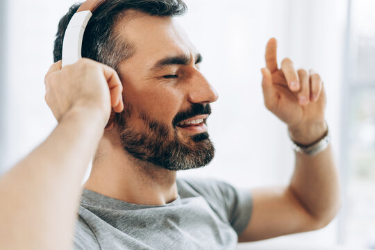 Portrait of happy handsome man listening music in headphones, sitting on comfortable sofa
