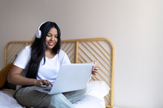 Latin woman working remotely from home using laptop and headphones - Powered by Adobe