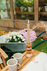 Candle burning on table with flowers in wheelbarrow greenhouse background outdoors