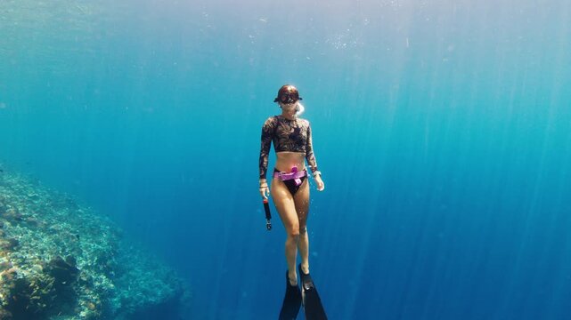 Underwater view of the woman freediver in sensual bikini exploring healthy coral reef in the tropical calm sea near the Alor island in Indonesia