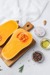 Butternut squash cut in half on wooden board with oil, salt, pepper and rosemary