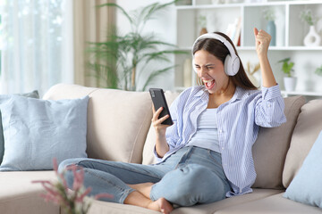 Obraz premium Excited woman in blue wearing headphone checking phone