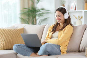 Happy woman in yellow wearing headphone watching media on laptop
