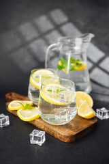 Lemonade with sliced lemon and fresh mint leaves served in glass jug on bright summer table with sunlight