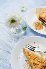 Napoleon cake slices layered with cream and puff pastry on white plates with flowers