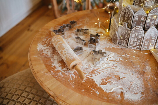 Wooden table with flour cookie cutters and gingerbread house baking prep.