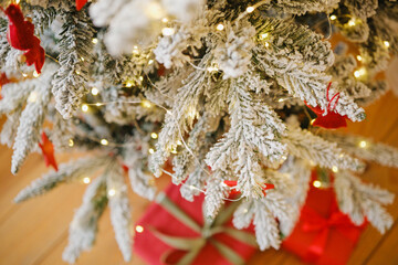 Snowy evergreen branches with glowing warm lights and red wrapped gifts below