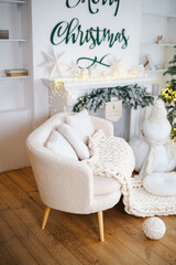 Naklejka premium Cozy cream armchair with warm knit blanket near decorated fireplace and Christmas tree