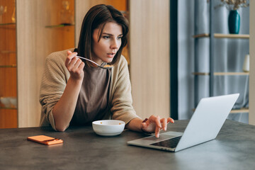 Woman multitasking, having breakfast while working remotely on laptop