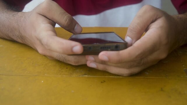 Footage displays hands using a smartphone on a table, showcasing mobile technology interaction. The clip emphasizes connectivity, communication, and digital lifestyle in a modern context.