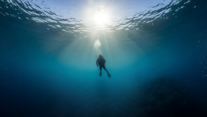 Sunlight breaking through the ocean surface illuminates a lone diver exploring the deep blue