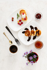 Cup of coffee and curd fritters with sour cream, berries and chocolate on the porcelain plates.