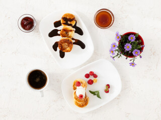 Cup of coffee and curd fritters with sour cream, berries and chocolate on the porcelain plates.