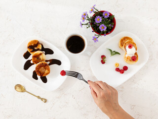 Cup of coffee and curd fritters with sour cream, berries and chocolate on the porcelain plates.