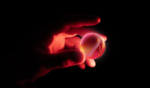 Warm glowing neon sphere held between illuminated fingers in darkness. Concept of digital energy, futuristic lighting design, abstract power symbolism, and creative tech visuals.