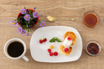Cup of coffee and curd fritters with sour cream and berries on the porcelain plates.
