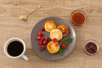 Cup of coffee and curd fritters with raspberries on the wooden background.