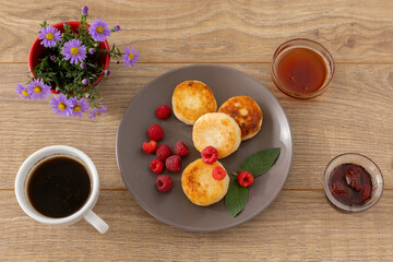 Cup of coffee and curd fritters with raspberries on the wooden background.
