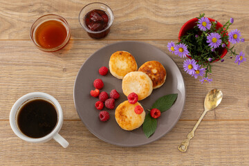 Cup of coffee and curd fritters with raspberries on the wooden background.