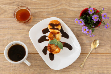 Curd fritters with chocolate and honey. Cup of coffee on the wooden background.