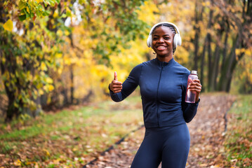 Fototapeta premium A runner stands on a running trail, looking relaxed and happy, with vibrant yellow and green leaves creating a lively autumn atmosphere around her.