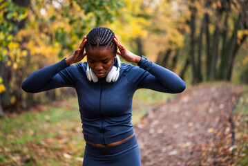 Young black woman is exercising in park in autumn. She is stretching her body before jogging.