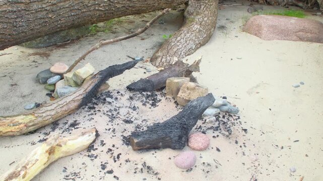 A place with an extinguished campfire on the seashore. A fire pit lined with sea pebbles. A campsite with old bonfire for tourists.