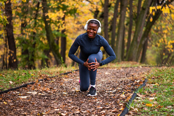 Young black woman is jogging in park in autumn and got injured. She has pain in her knee. 