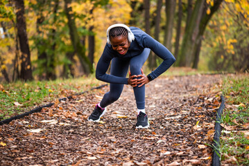Young black woman is jogging in park in autumn and got injured. She has pain in her knee. 