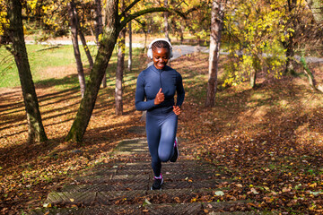 Amid warm autumn tones, a runner makes her way up a path lined with trees, appearing energized and happy during her outdoor workout.