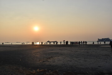 Obraz premium Coastal sunset scene with silhouetted people and ships.