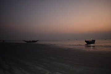 Anchored fishing boats on a dark, moody beach at twilight.