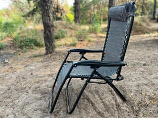 Portable recliner chair standing on sand in forest