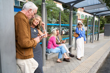Seniors using smartphones at bus stop waiting for public transport