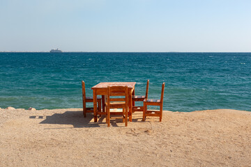 Wooden table and chairs on a beach by the Mediterranean Sea.