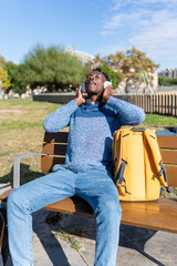Fototapeta premium African American man relaxing on park bench listening to music with headphones