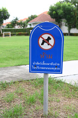 No Dog Pooping sign on a neatly maintained lawn with a crossed-out dog symbol stands next to a sidewalk in a residential area