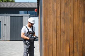 Construction worker preparing drill next to wooden wall