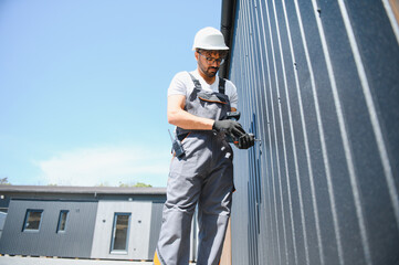 Construction worker using cordless drill installing metal siding on prefabricated building
