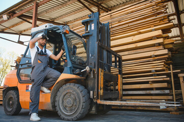 Warehouse worker driving forklift by lumber stacks